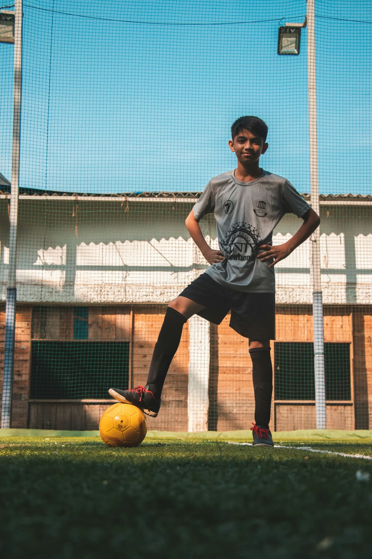 Jovem atleta com o pé apoiado na bola em um campo de futebol